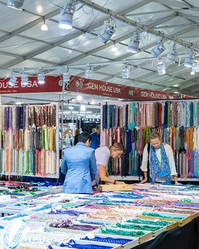 Fabric and bead vendor booths with shoppers under a white show tent