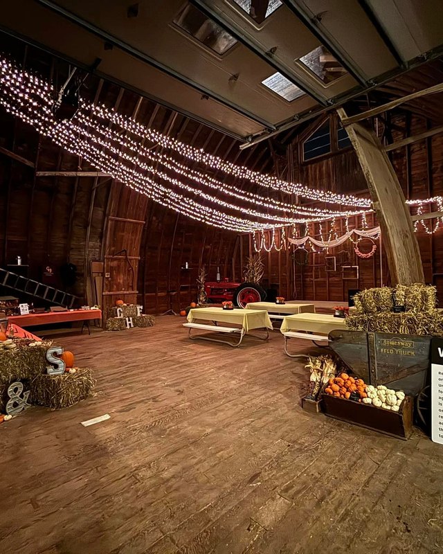 Barn interior at Coleman Hay Farms decorated with string lights, hay bales and pumpkins.