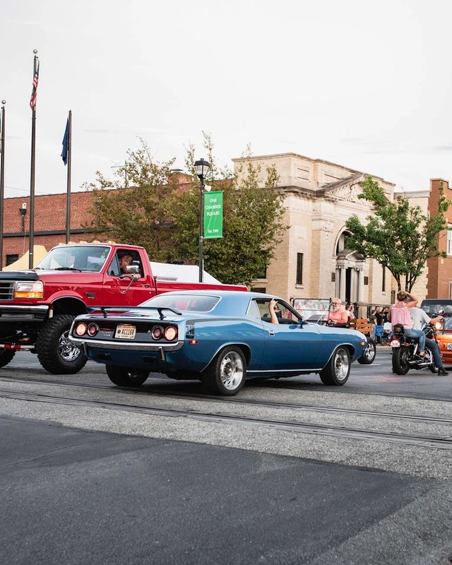 Classic cars and a red truck cruising a downtown Seymour street during Scoop the Loop, with spectators along the curb.