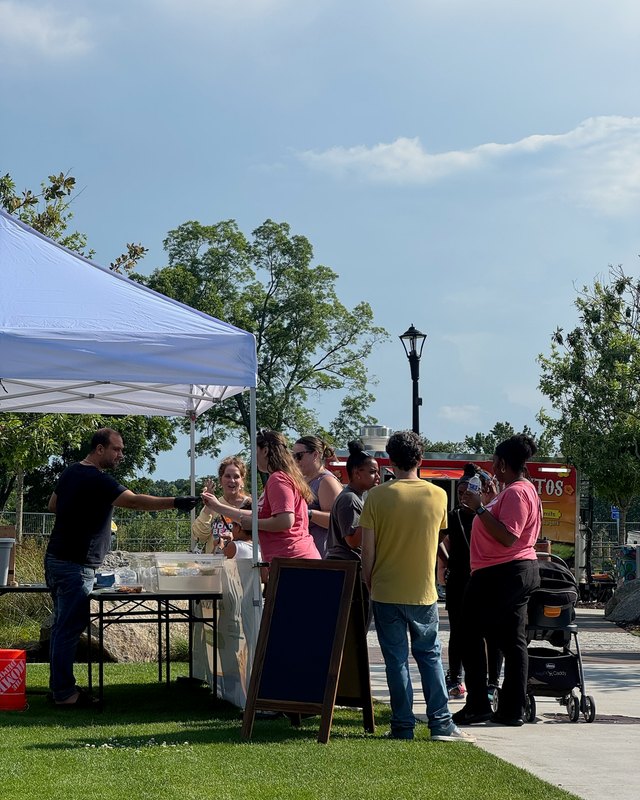 Shoppers gathered at a vendor table under a blue-and-white canopy on the grass at Douglasville Town Green