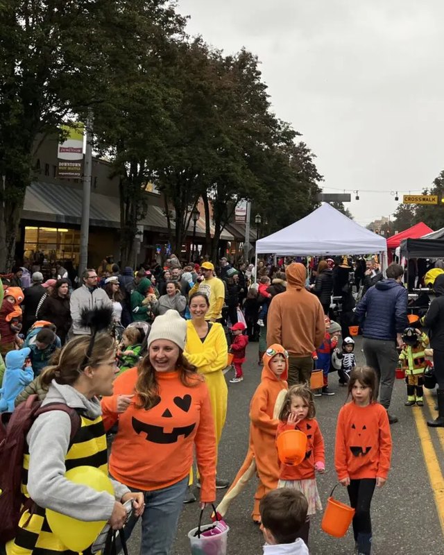 Costumed families and crowds walking past tents on a street at the West Seattle Harvest Festival.
