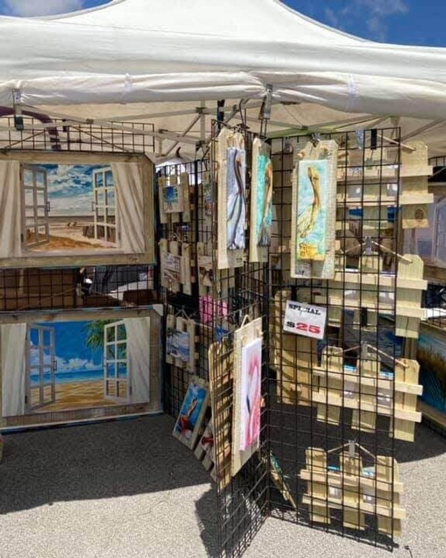 Art booth with framed paintings and canvases displayed under a white tent