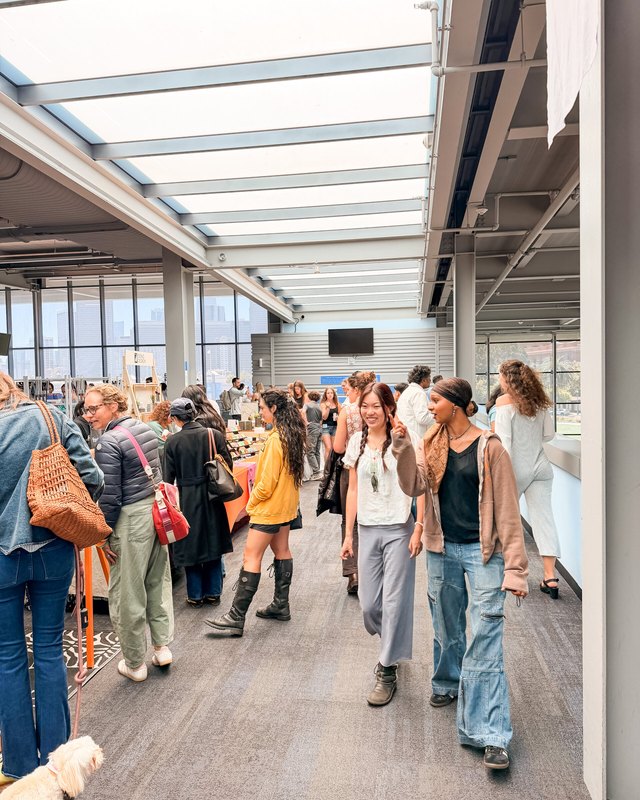 Shoppers walking through a bright indoor market hall with vendor booths under a skylit ceiling