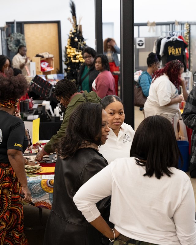 Shoppers browsing vendor booths with holiday lights at an indoor market.