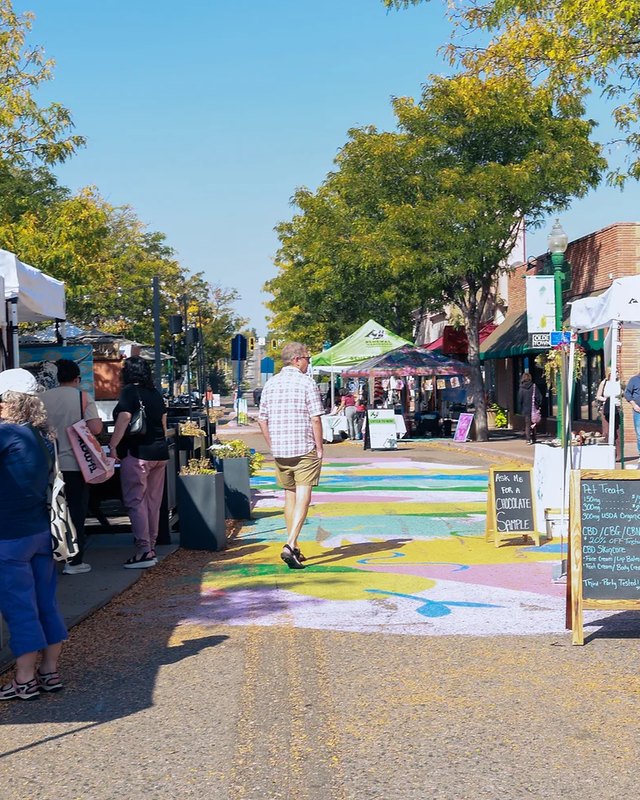 Market street lined with white vendor tents and booths under trees at the Jackalope fair in Olde Town Arvada