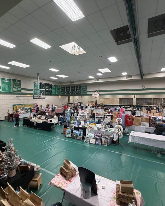Shoppers and vendor tables fill the gym at the Holy Infant holiday boutique under ceiling lights.