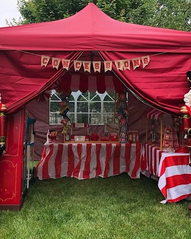 Red tent booth with nutcracker statues and striped tables of goods on a grassy lawn
