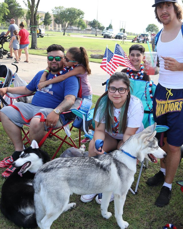 Families and a dog relaxing with flags at the Red, White & Blue Blast in Sachse on a grassy park lawn.