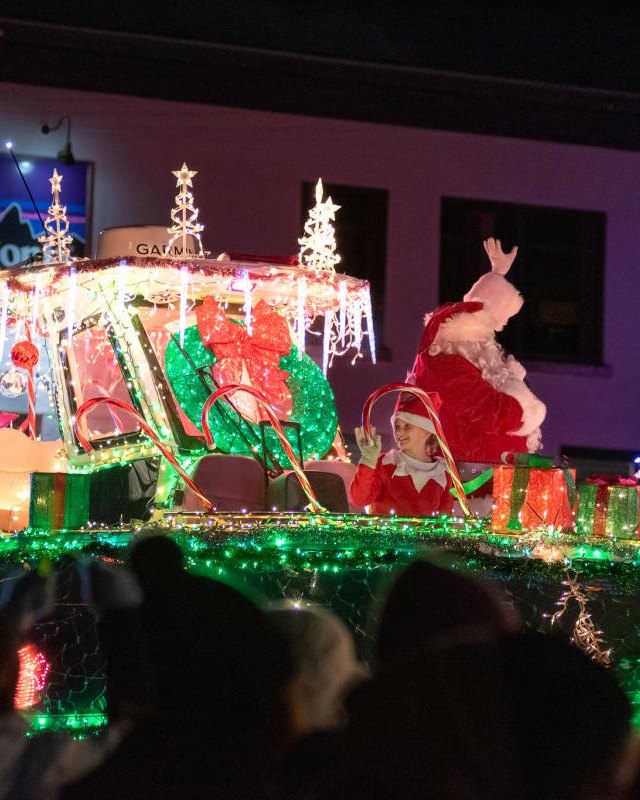 Brightly lit holiday parade float with Santa and reindeer, watched by a crowd at night in Freeport.