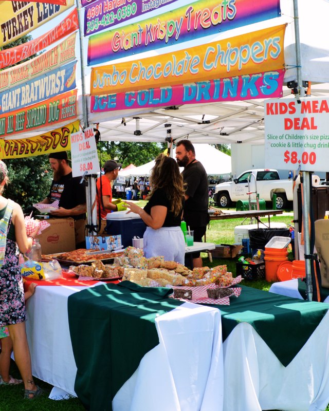 Food vendor booth with menu signs and people lining up at Lincoln Park during the Greeley Arts Picnic.